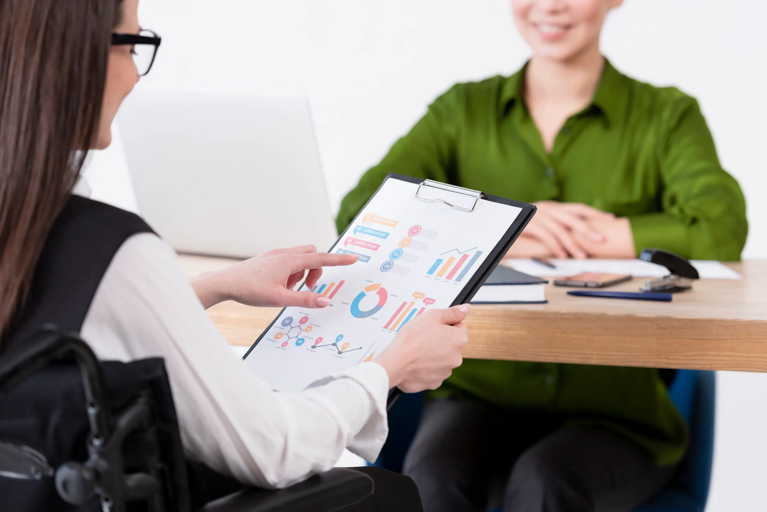 A person in a wheelchair reviewing bar and pie charts on a clipboard across from a colleague
