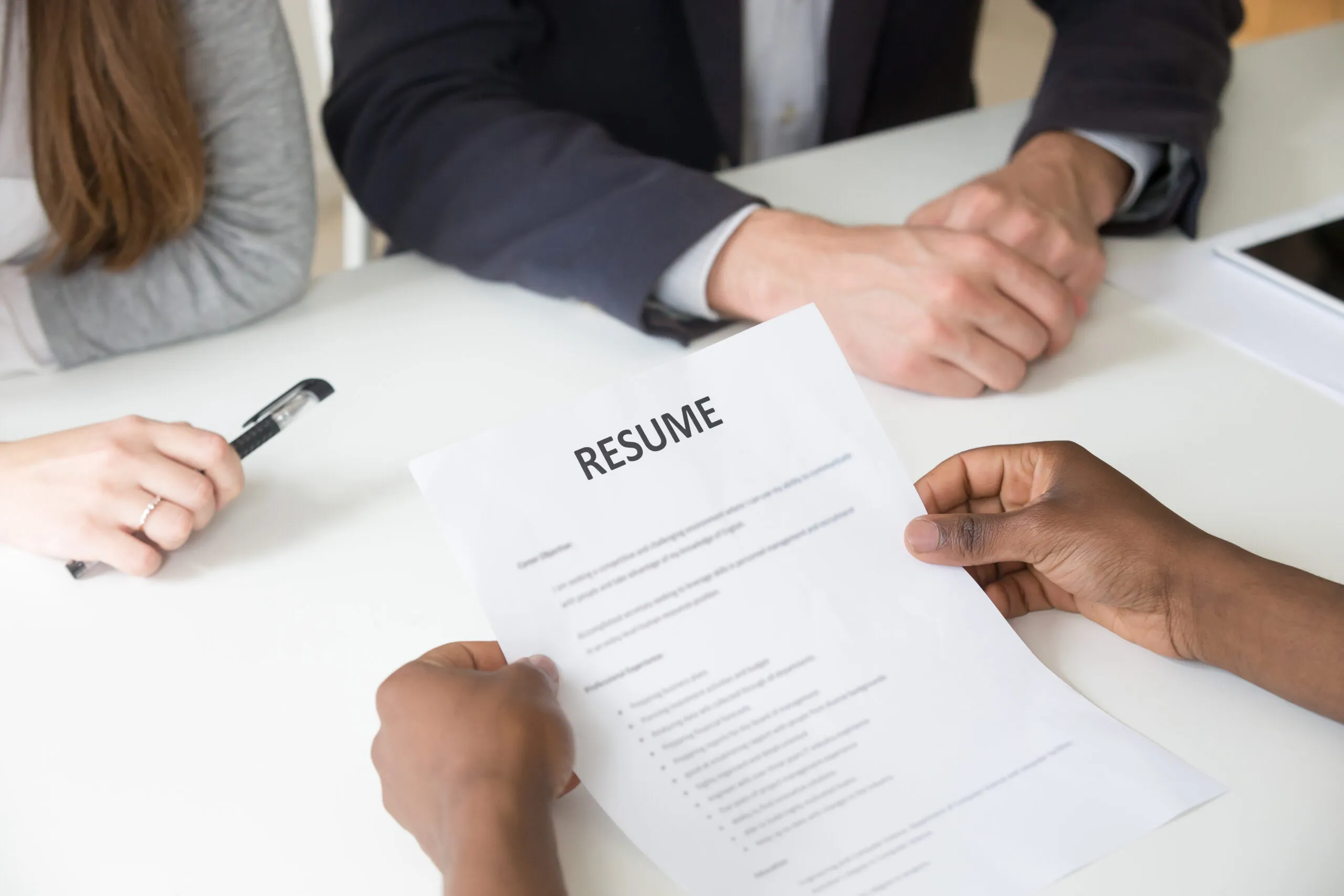 Two interviewers reviewing a printed resume handed across a table